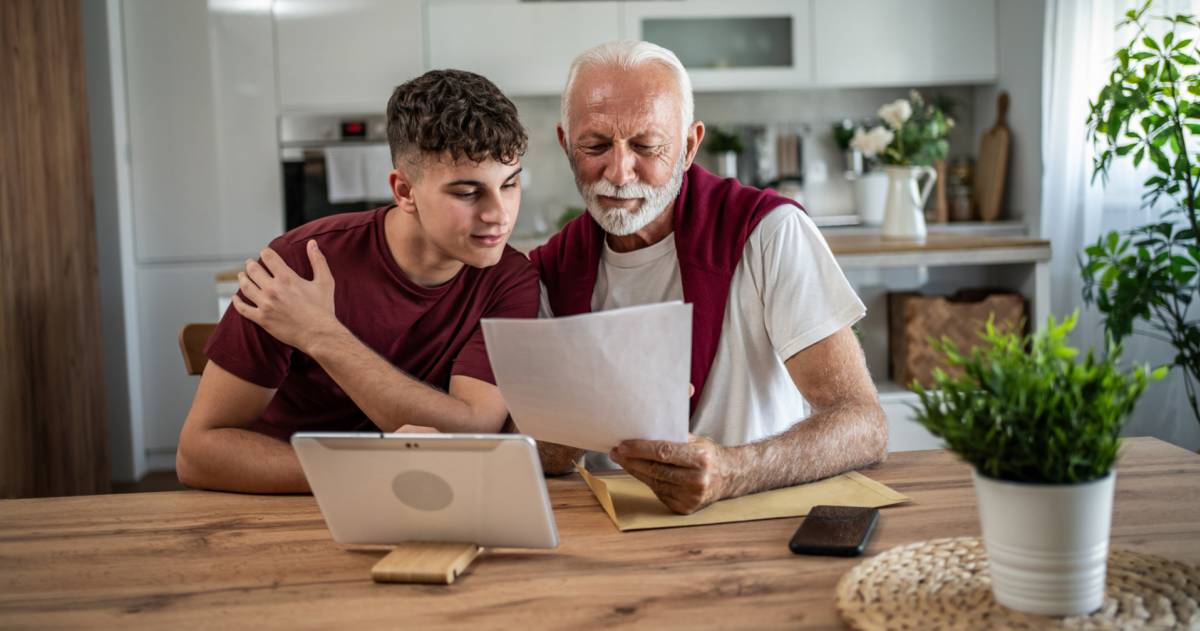 Grootvader en kleinzoon bestuderen samen thuis financiële documenten.
