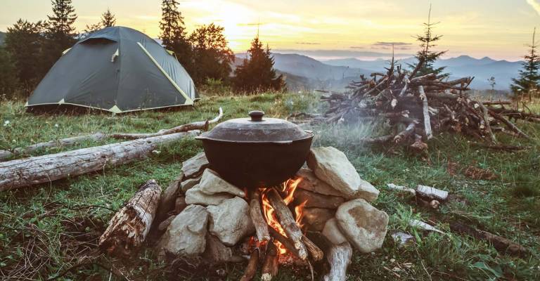 Een toerist is aan het kamperen met een tent en een kampvuur in het bos en de bergen