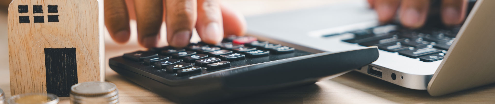 Een man is aan het rekenen op een rekenmachine met op de voorgrond een huisje en munten